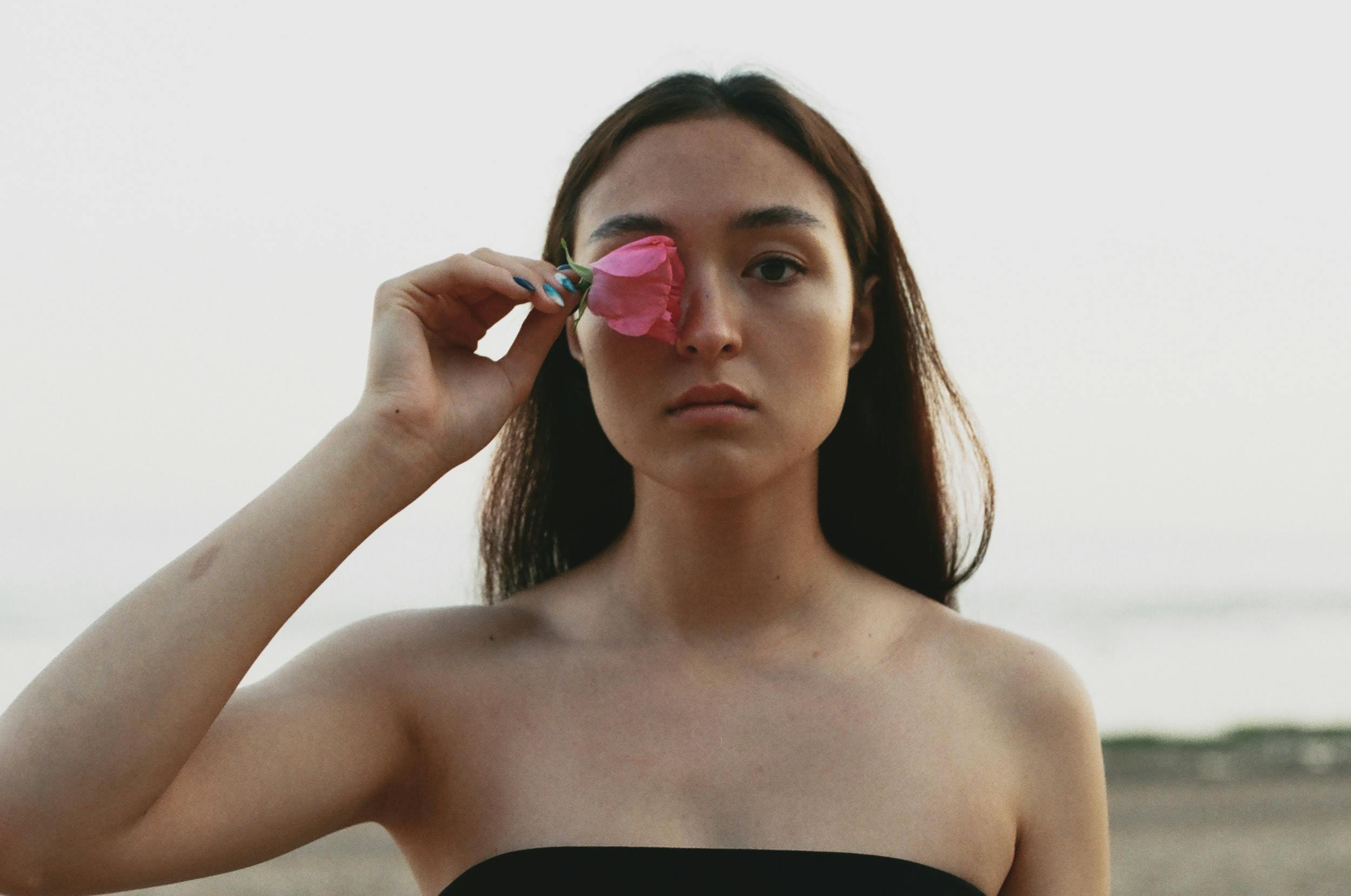 A serene portrait of a woman holding a pink flower, showcasing natural beauty and tranquility outdoors.