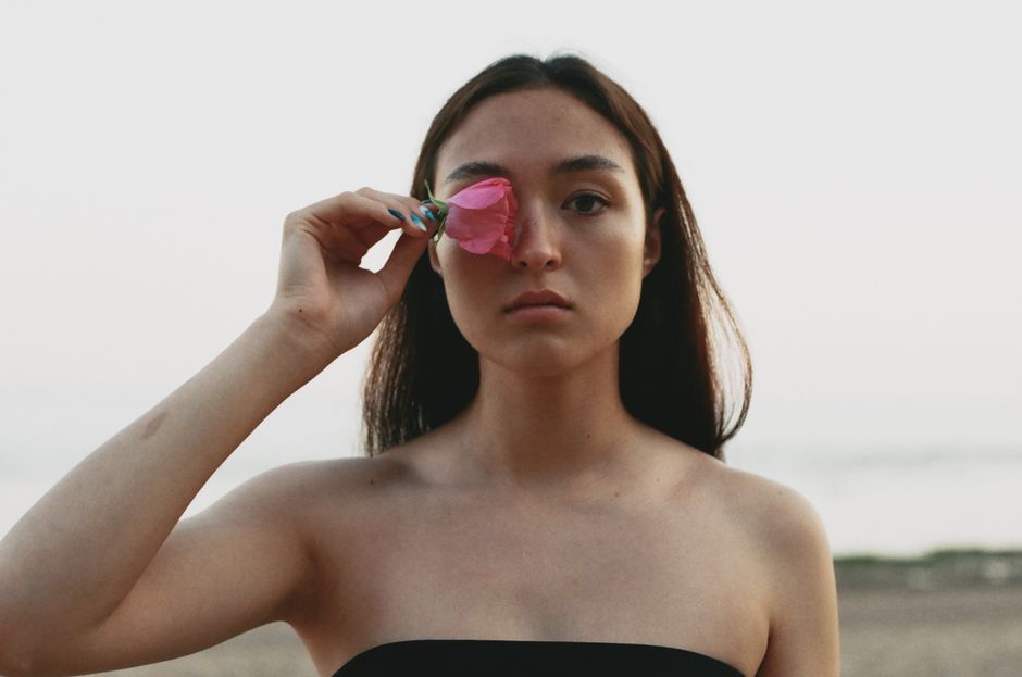 A serene portrait of a woman holding a pink flower, showcasing natural beauty and tranquility outdoors.