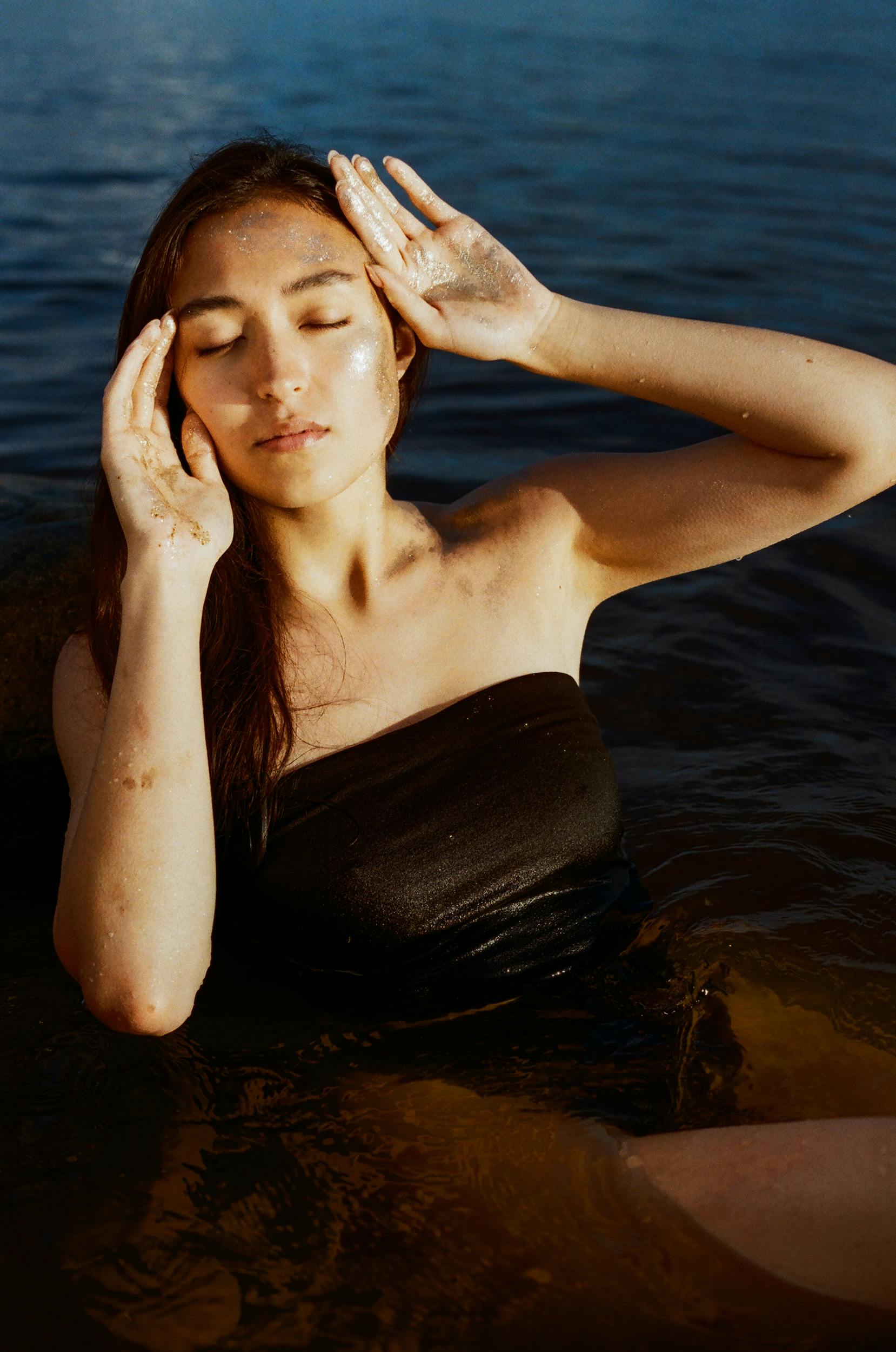 A woman enjoying a peaceful moment in the water, basking in natural sunlight with eyes closed.