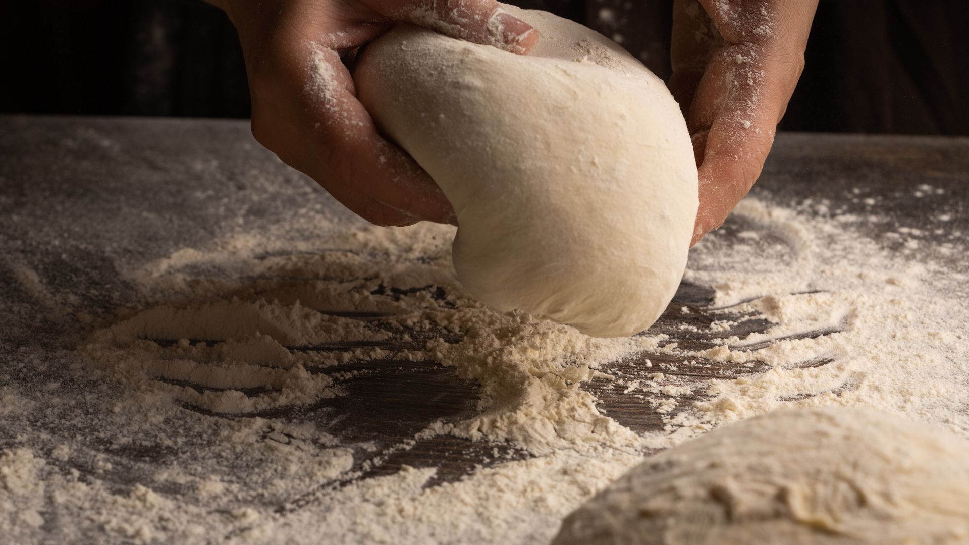 A baker’s hands shaping dough on a floured bench