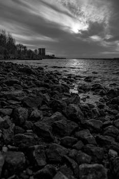 A striking black and white coastal scene featuring a rocky shore and dramatic clouds over the sea.