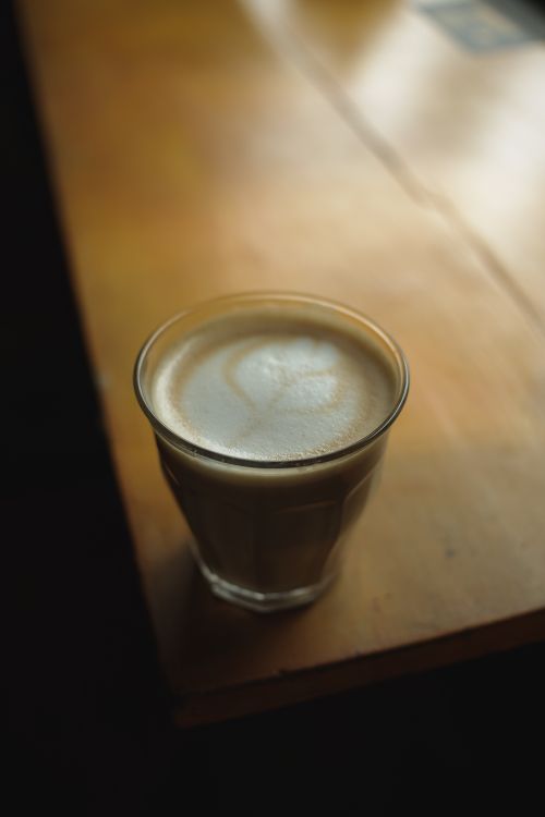 Free A creamy cappuccino in a glass sits on a sunlit wooden table, perfect for a cozy coffee moment. Stock Photo