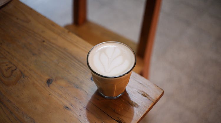 A Glass Of Creamy Coffee On The Edge Of The Wooden Table