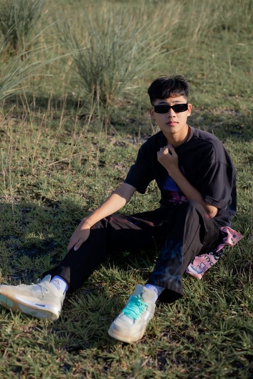 Free Stylish young man wearing sunglasses seated on grass in casual attire. Stock Photo