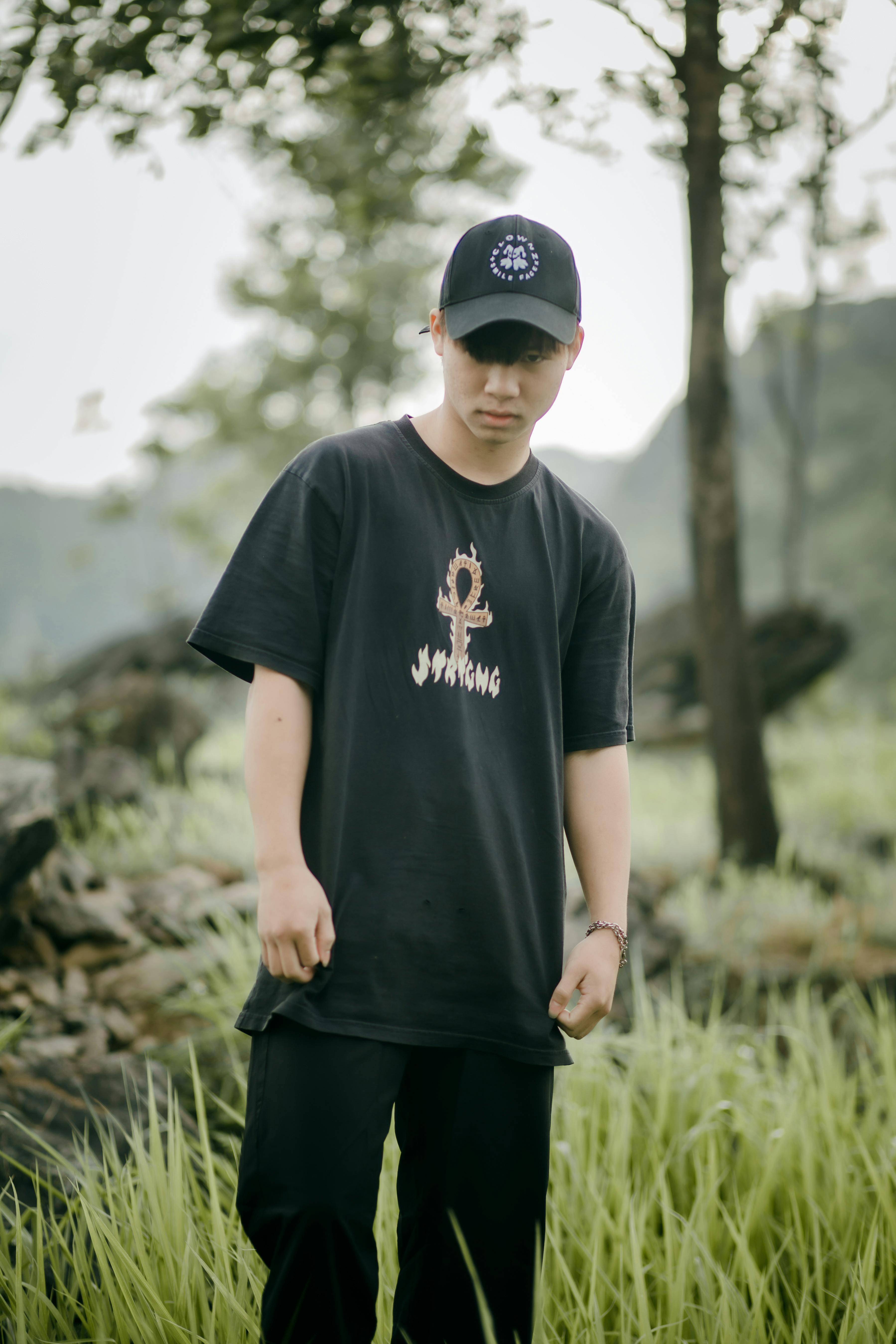 Young man in casual streetwear outfit poses outdoors in a lush natural setting.
