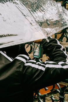 Unrecognizable person using a smartphone under a transparent umbrella on a rainy day.