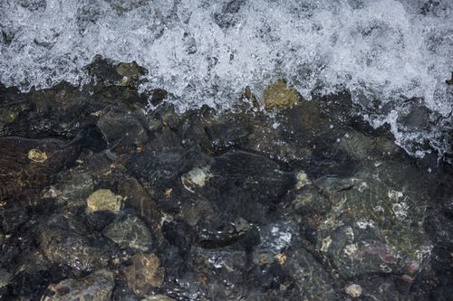 Free Close-up of waves splashing over rocks and stones at a pebble beach with clear water. Stock Photo