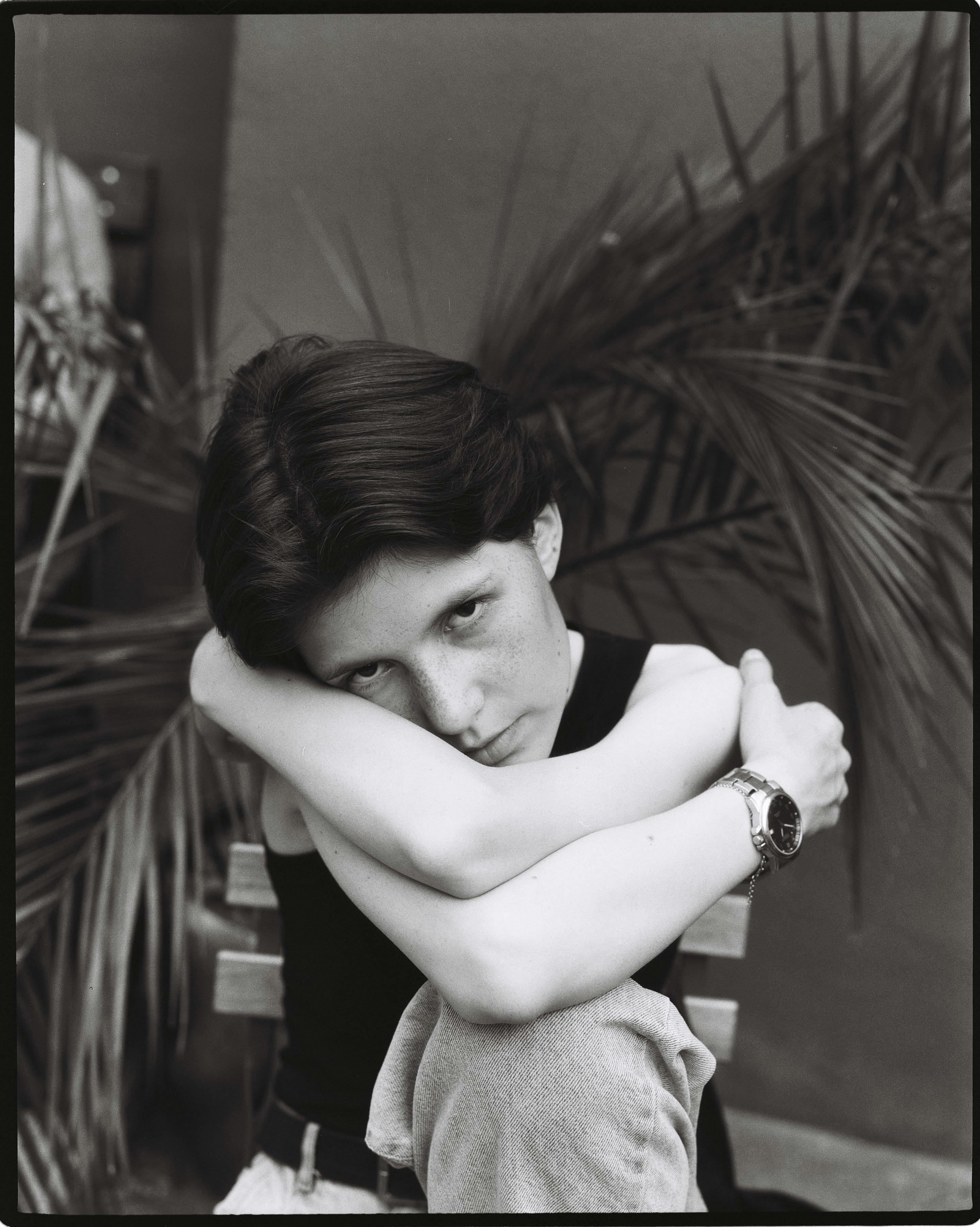 A black and white portrait of a woman sitting indoors with arms crossed.
