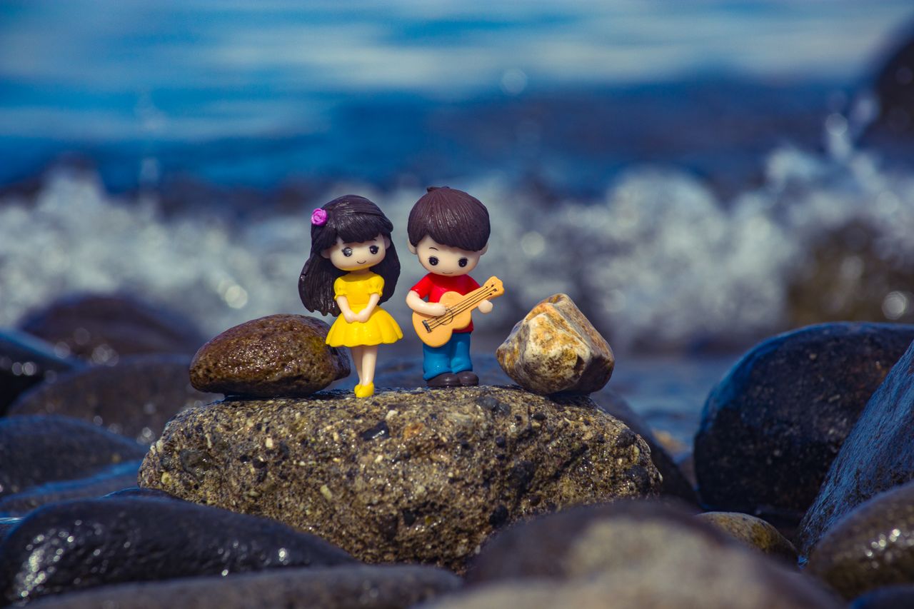 miniature toy figures of a boy and girl on rocks by the sea with a blu