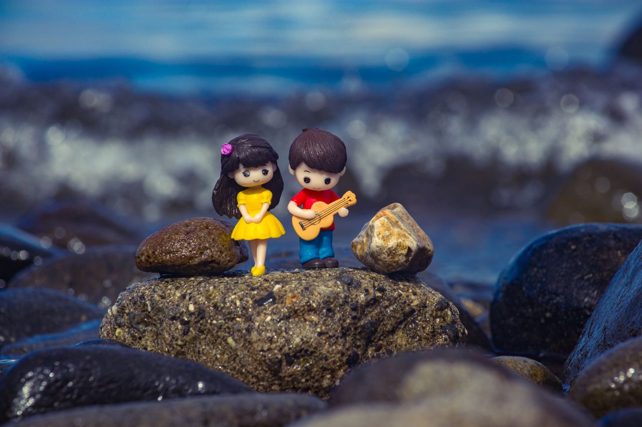 a cute pair of miniature figurines on a mossy rock by the ocean shore