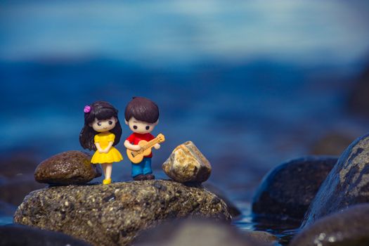 Miniature figures of a couple standing on rocks by the water's edge.