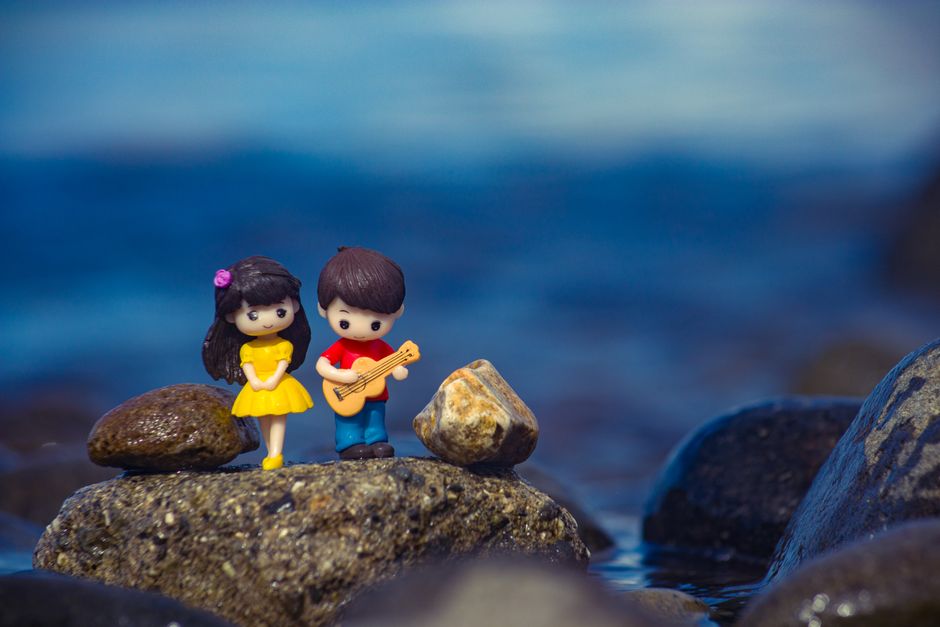 Miniature figures of a couple standing on rocks by the water's edge.