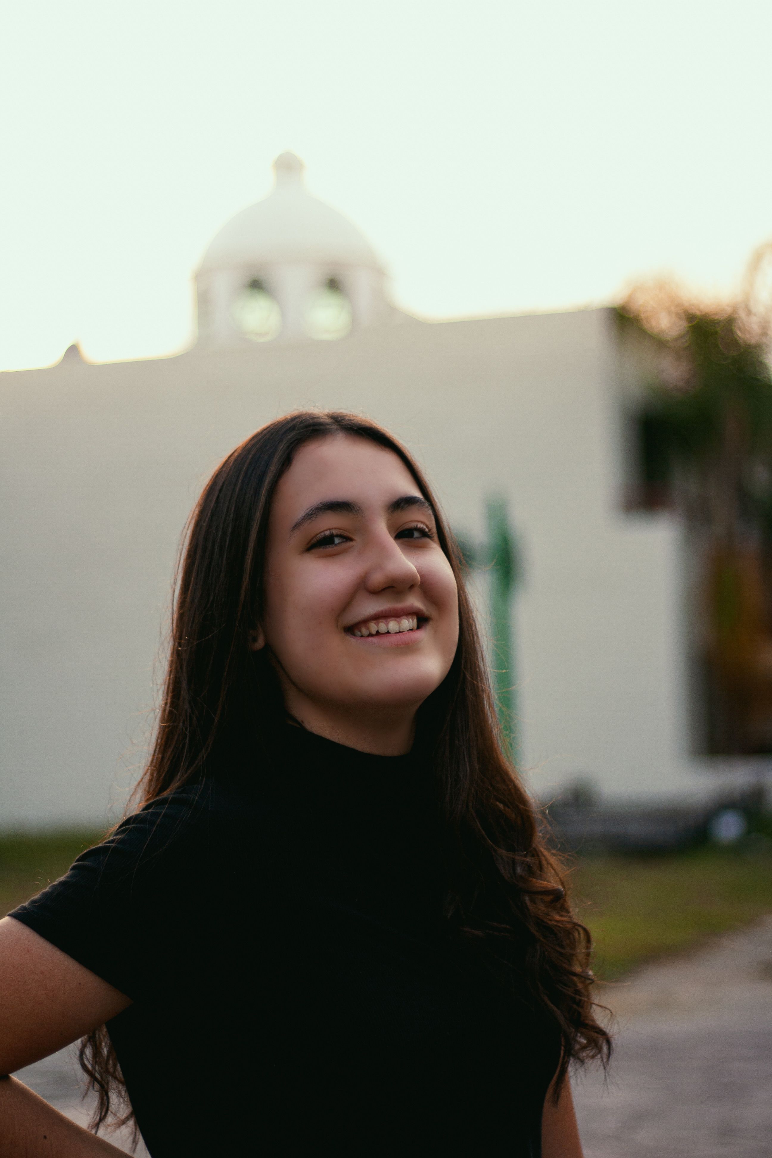 Portrait of a happy woman smiling outdoors near a dome structure during the day.