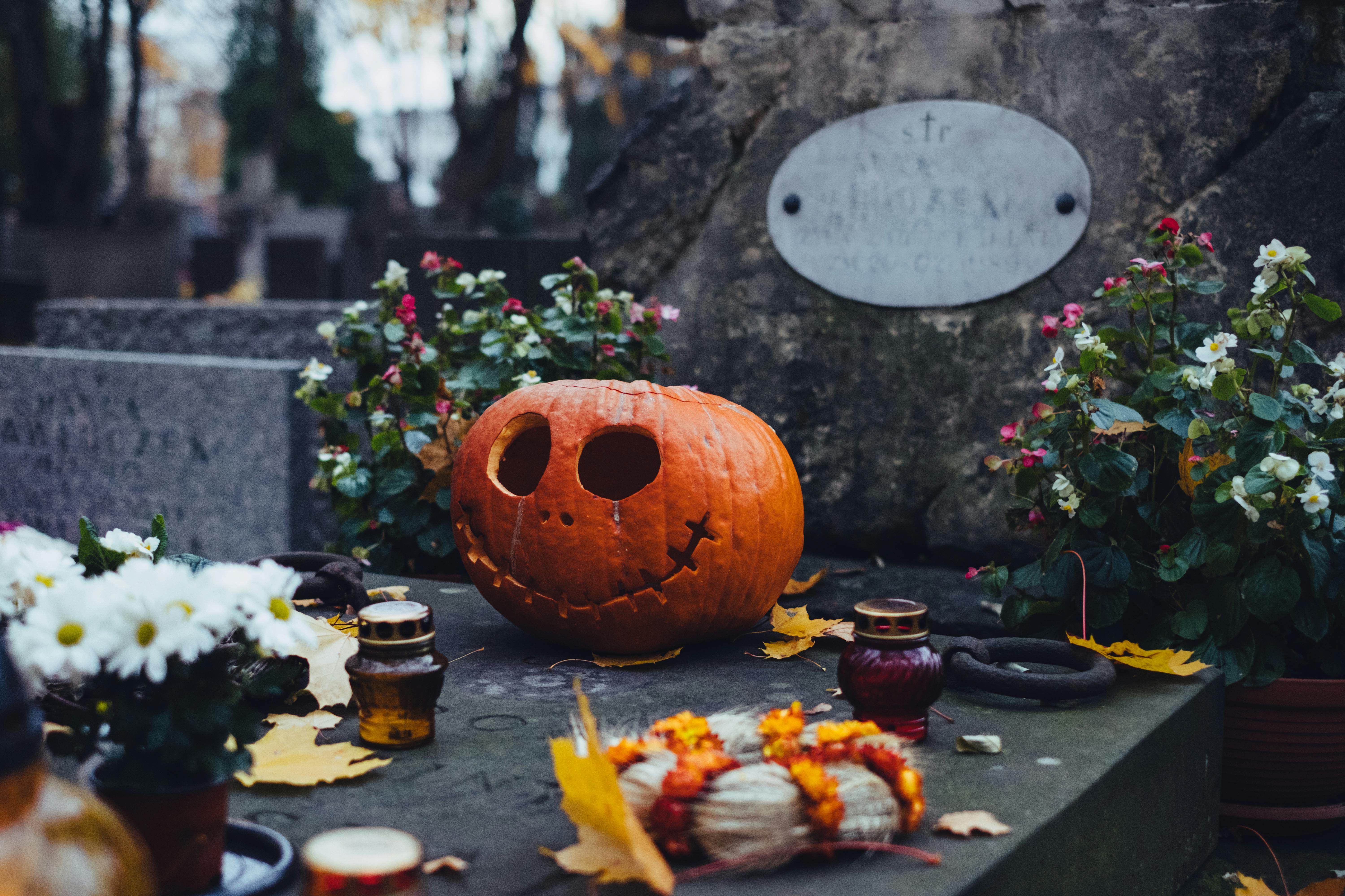 A spooky jack-o'-lantern on a grave surrounded by flowers and candles in a Warsaw cemetery.