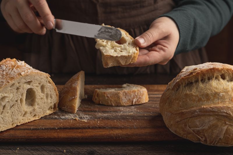 Close-up of hands spreading butter on slices of rustic artisan bread, showcasing texture and freshness.