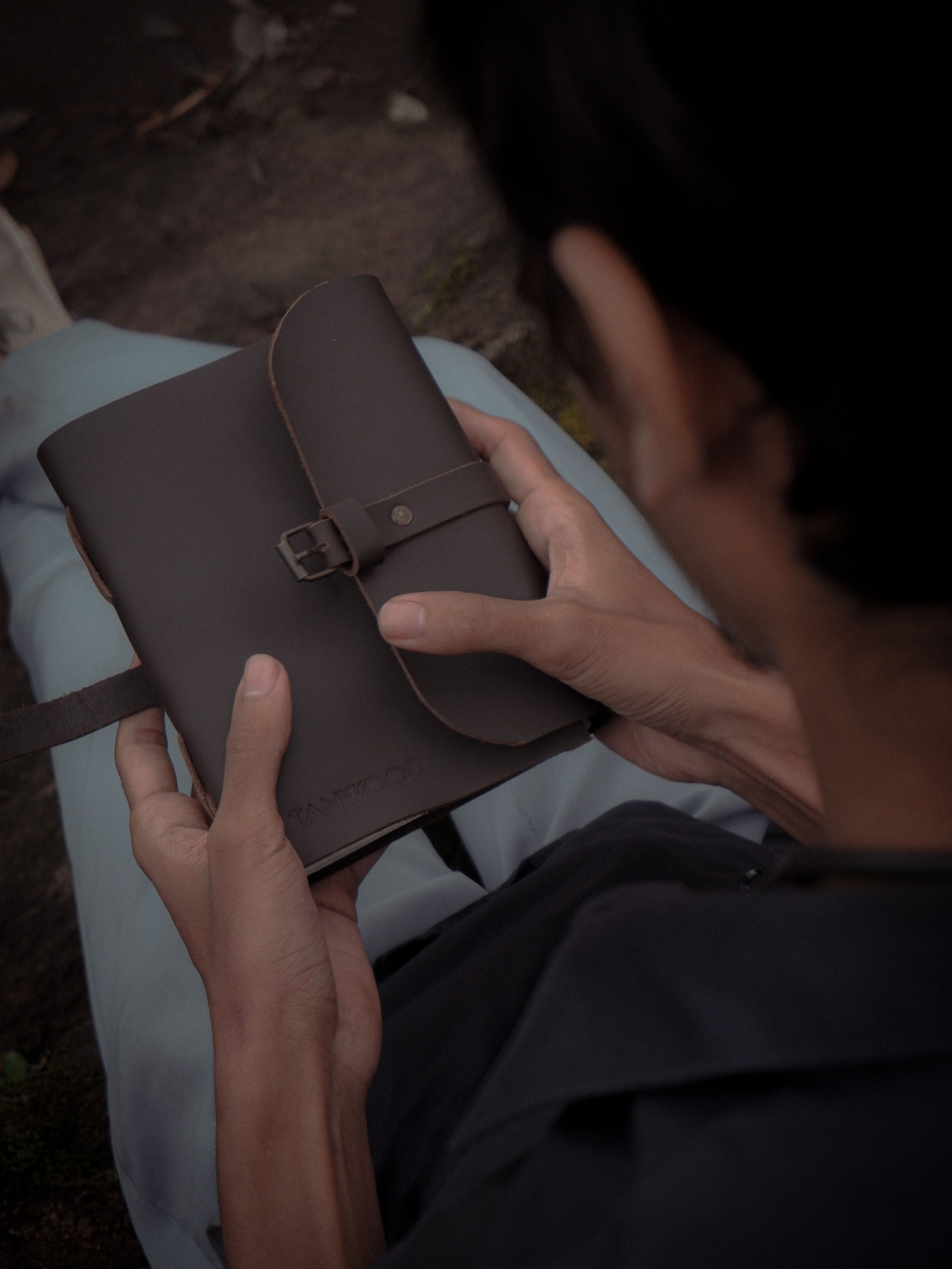 Unrecognizable person sitting outdoors holding a brown leather diary in their hands.