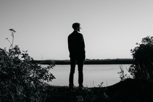 Free Silhouette of a man standing by a lake, thoughtfully gazing into the distance. Stock Photo