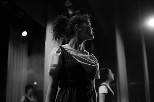 A Woman Wearing Striped Dress and White Shirt Lit by a Spotlight