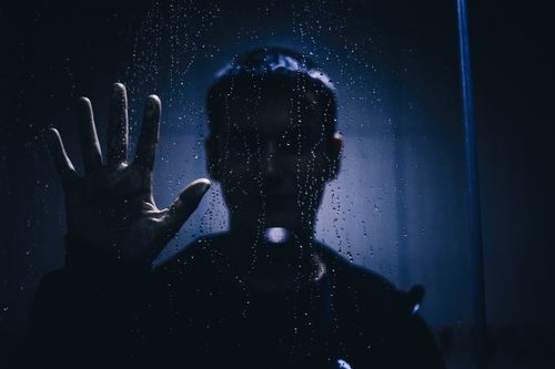 Free Silhouette of a person with hand against a rain-covered glass, evoking mystery and introspection. Stock Photo