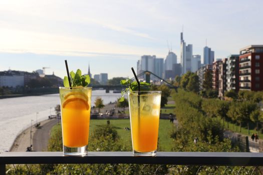 Two vibrant cocktails with ice and mint overlooking the Frankfurt cityscape on a sunny day.