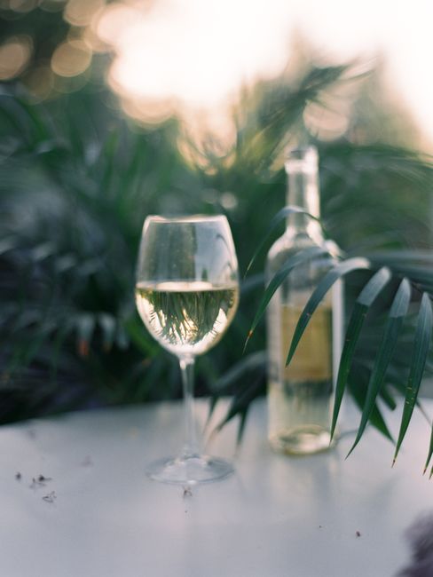 A sophisticated glass of white wine with a bottle in a lush tropical setting.