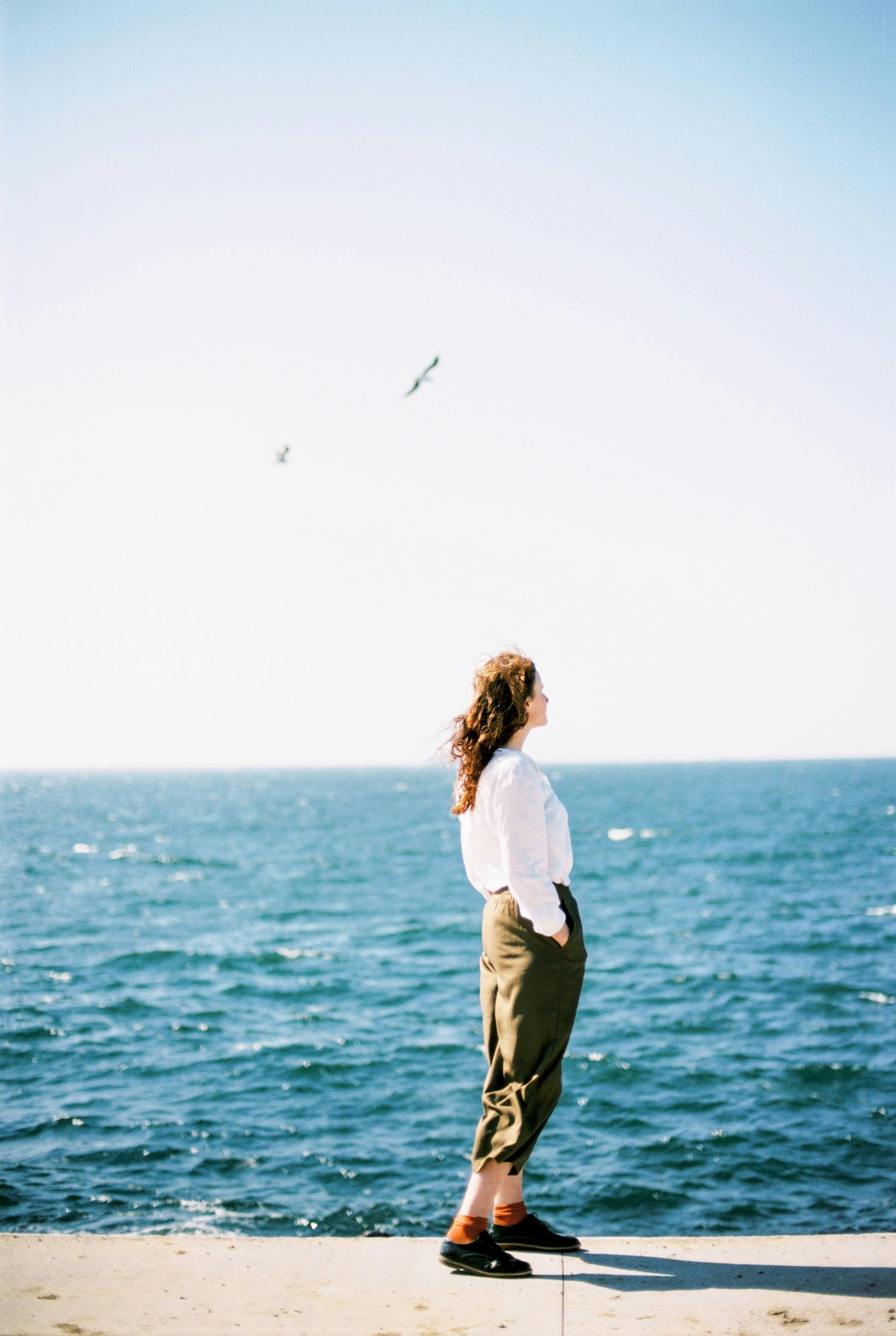 Woman in white shirt standing by the ocean under a clear, sunny sky.