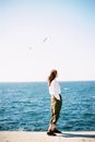 Woman in White Long Sleeve Shirt and Black Pants Standing on Rock Near Sea
