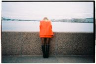 Woman in Orange Dress Standing on Gray Concrete Wall Near Body of Water