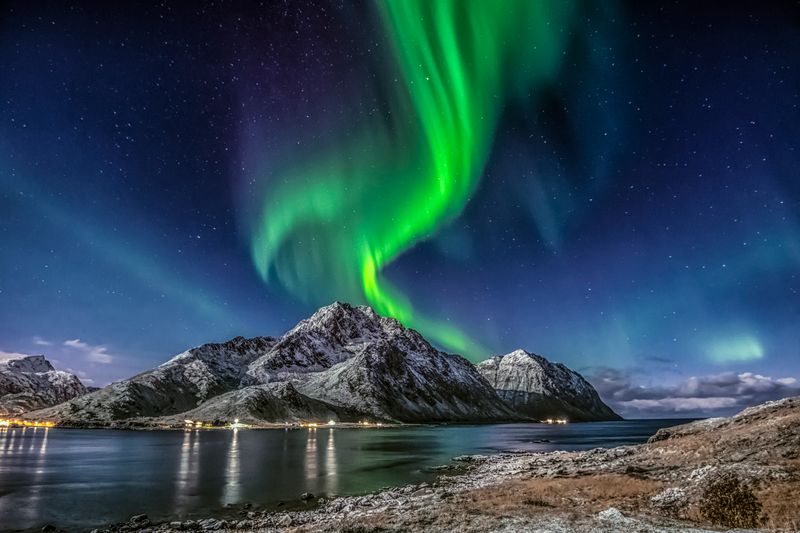 Aurora boreală verde deasupra muntelui acoperit cu zăpadă