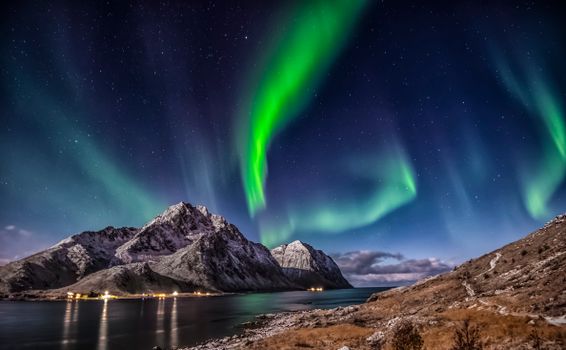 Stunning aurora borealis illuminating snowy mountains and sea in Nordland, Norway.