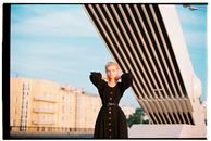 Woman in Black Long Sleeve Dress Standing Near White Concrete Building
