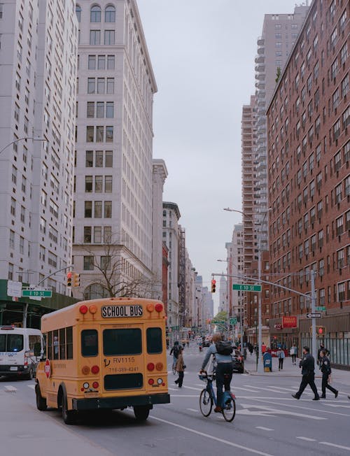 Free Yellow School Bus Traveling the Road Near High Rise Buildings Stock Photo