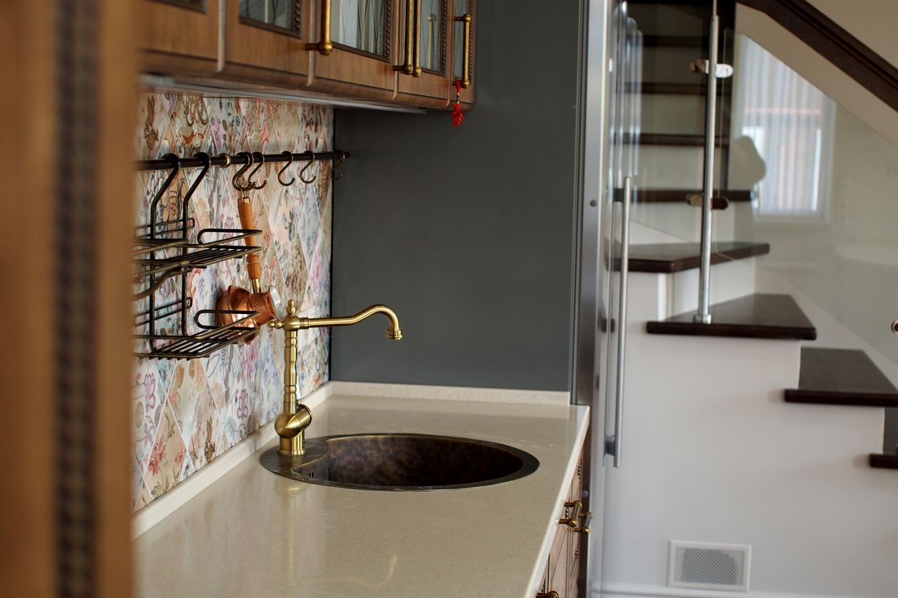 Gold faucet with a dark round bar sink beside a staircase