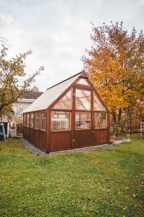 Free A rustic wooden greenhouse surrounded by vibrant autumn foliage, ideal for gardening enthusiasts. Stock Photo