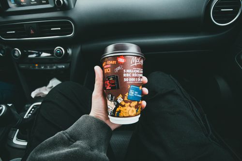 Free Close-up of a hand holding a McCafé coffee cup inside a car, capturing the cozy and casual travel vibe. Stock Photo