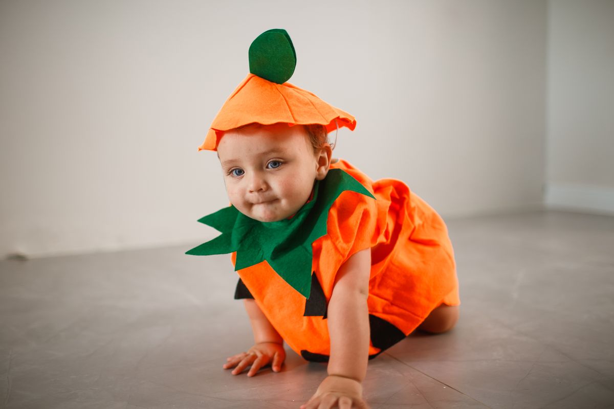Baby in an orange pumpkin outfit crawling on the floor