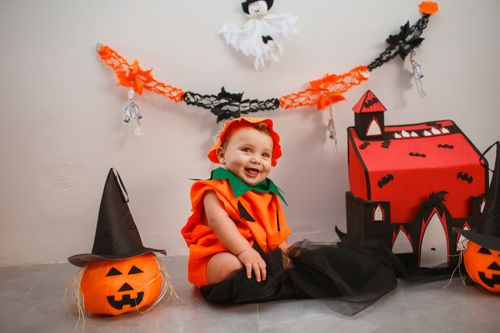 Free Cute baby dressed as pumpkin surrounded by Halloween decor, smiling indoors. Stock Photo