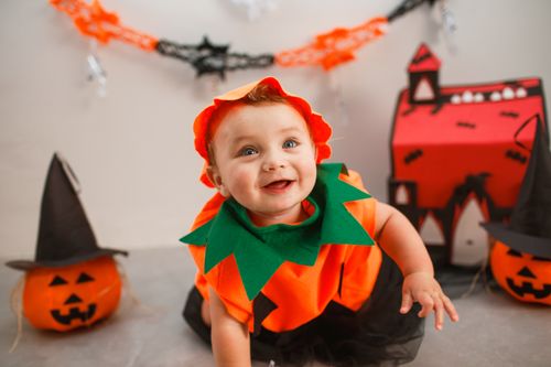 Free Cute baby dressed as a pumpkin celebrating Halloween indoors. Stock Photo