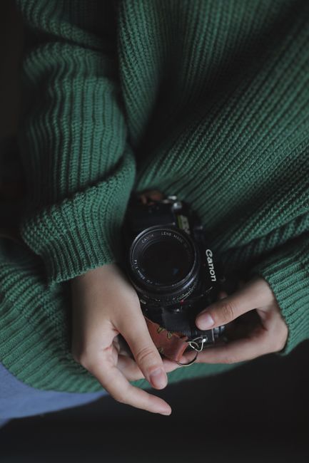 Close-up shot of hands holding a vintage camera with a green knitted sweater.