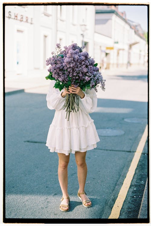Woman in White Dress Holding Bouquet of Purple Flowers