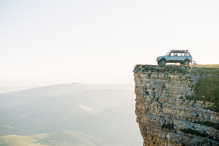 A Car Parked On The Cliff Of A Mountain Under White Sky