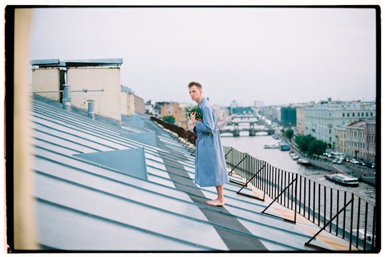 A Man In Blue Robe Standing On The Roof Of A House While Looking At The Camera