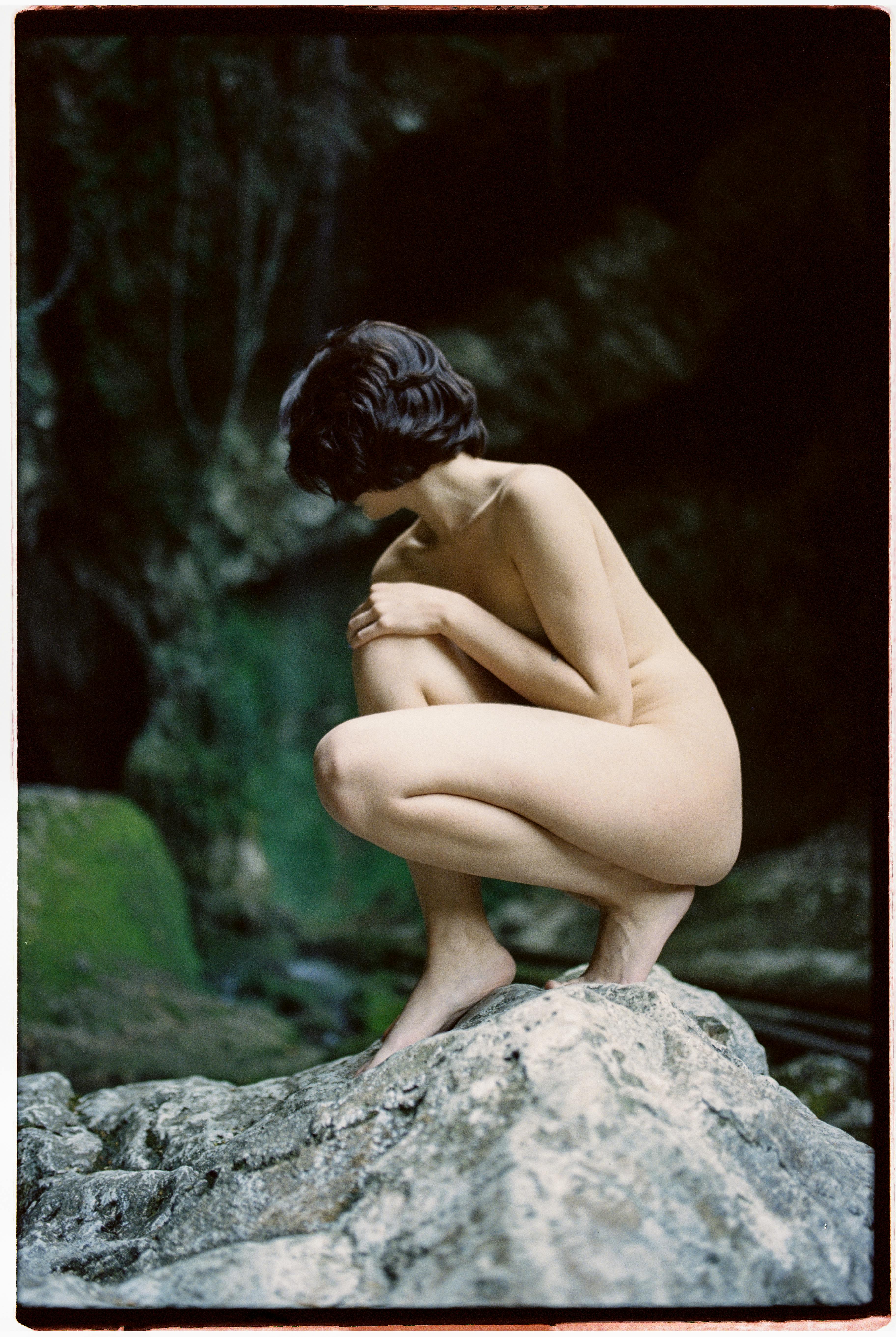 a naked woman sitting on big rock