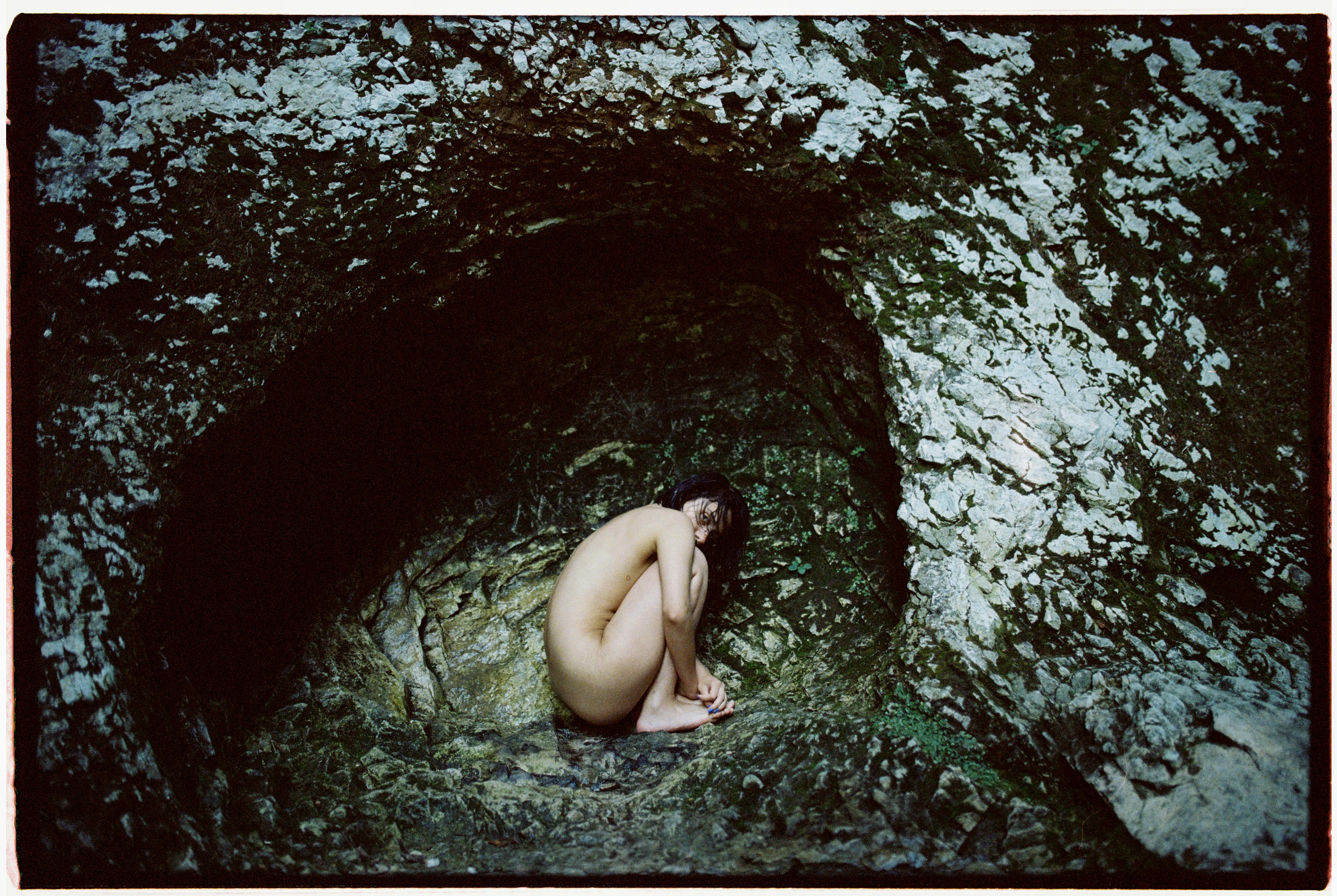 naked woman curled in a rocky cave