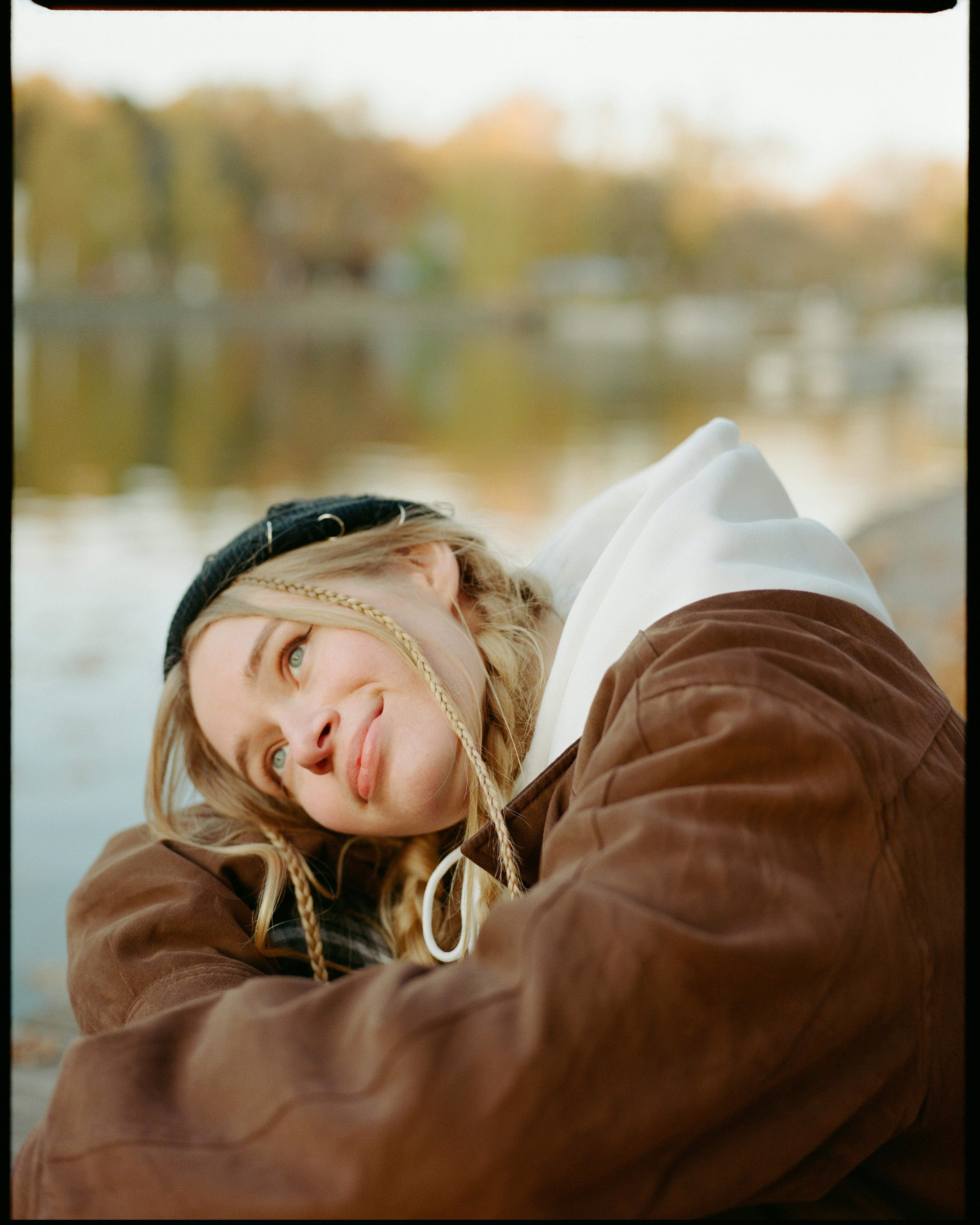 A happy woman with braids wearing a beanie and brown coat by the river in Moscow, Russia.