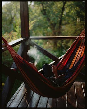 Adult man smoking in a hammock on a wooden porch in Chepelyovo, Russia.