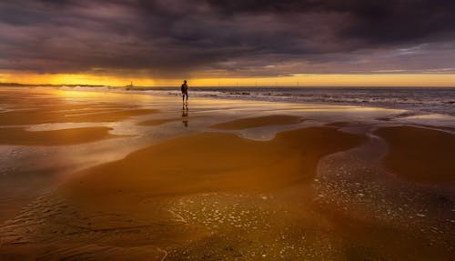 A Person Walking on a Beach during Sunset