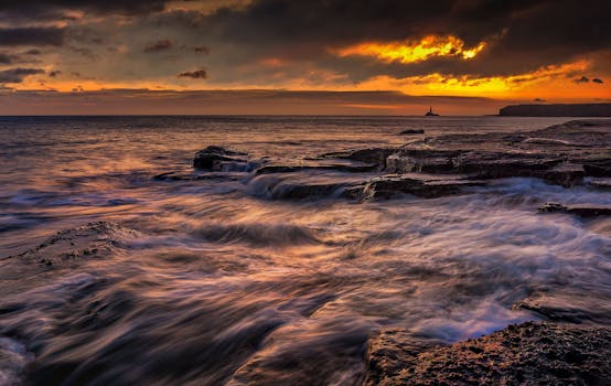 Stunning sunset over a rocky seascape with vivid orange and gold skies and strong ocean currents.