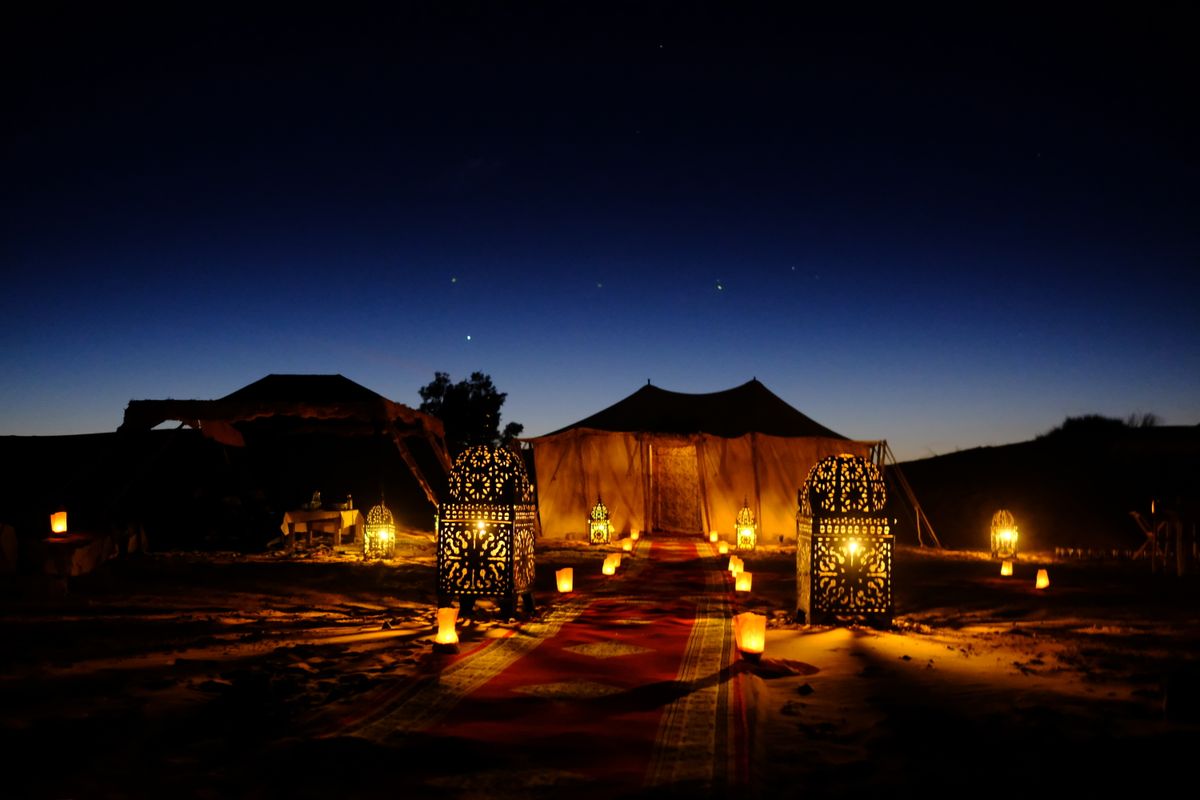Illuminated tents with lanterns at twilight in Egypt's desert, stars beginning to appear overhead