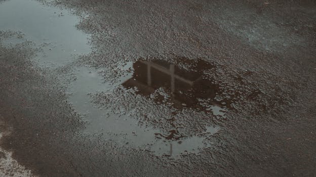 Rain puddle on asphalt with reflection of structure, creating a moody scene.